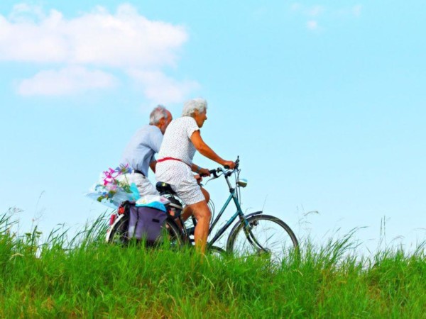 Kaksi iäkkäämpää henkilöä pyöräilemässä kauniilla säällä.